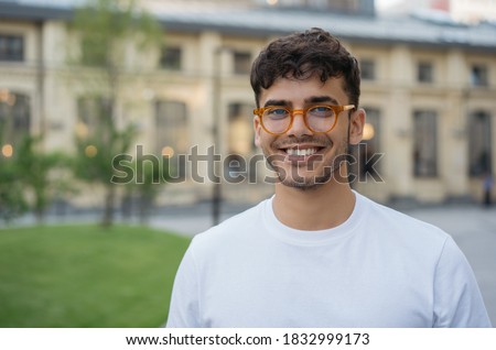 Authentic portrait of young successful Indian man wearing stylish eyeglasses, standing on the street. Handsome asian model posing for pictures, looking at camera, smiling