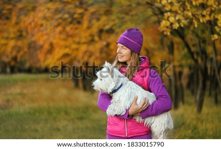 Side view picture of a sportive woman holding her dog in hands