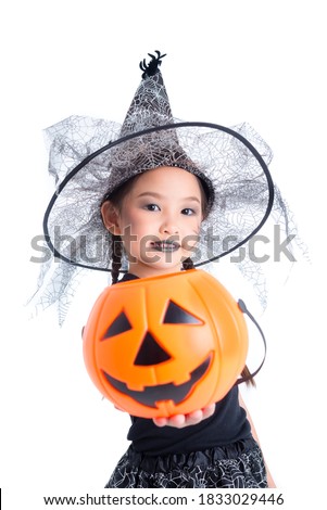 Cute Asian girl in halloween costume holding pumpkin bucket and smiling over white background.