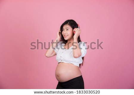 Beautiful pregnant Asian woman listening to music from
Headphones comfortably On a ฺpink background , Expectation of young mothers, pregnancy pictures and childbirth