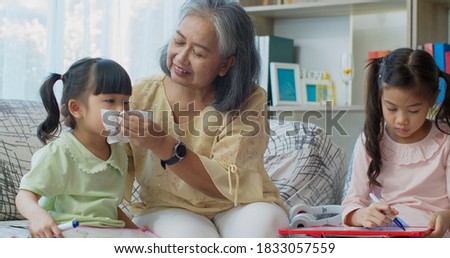 Asian grandma take care and used a tissue and taught her granddaughter to blow her nose while they joyful with drawing on white board in living room