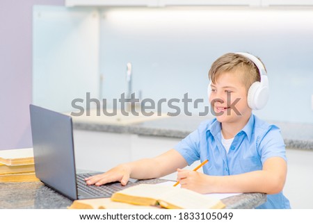 The boy is engaged in training while sitting at home looking into the laptop screen with headphones on his head with a happy smile. Distance education during a pandemic, distant.
