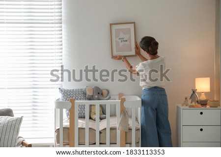 Decorator hanging picture on wall in baby room. Interior design