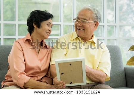 Senior Asian elderly couple in home casual outfit with happy smiling emotion sitting in living room bring back to the past in memory from old picture together