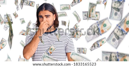 Young handsome man wearing casual clothes smelling something stinky and disgusting, intolerable smell, holding breath with fingers on nose. bad smell