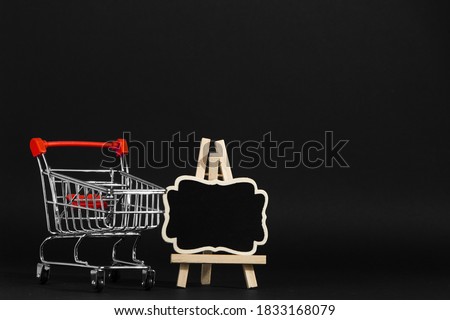A frame on a stand and shopping cart on a black background, a blank for the design, concept. Copy space.