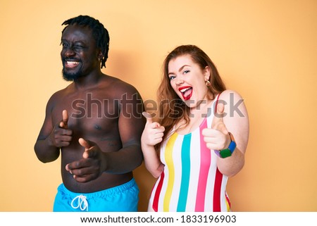 Interracial couple wearing swimwear pointing fingers to camera with happy and funny face. good energy and vibes. 