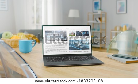 Advanced Modern Ultrabook Laptop with Technology and Sports News Feed on Screen Display Standing on the Desk in the Bright Cozy Living Room.