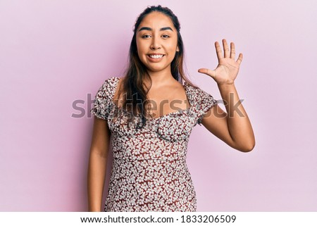 Young latin woman wearing casual clothes showing and pointing up with fingers number five while smiling confident and happy. 