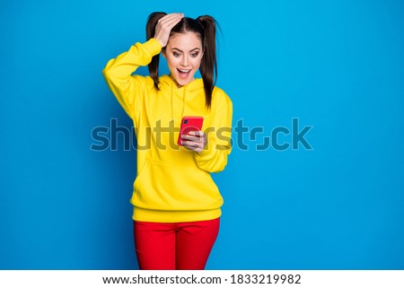 Photo of funny shocked lady two tails hold telephone popular blogger read post blog positive comments overjoyed wear casual yellow hoodie red trousers isolated bright blue color background