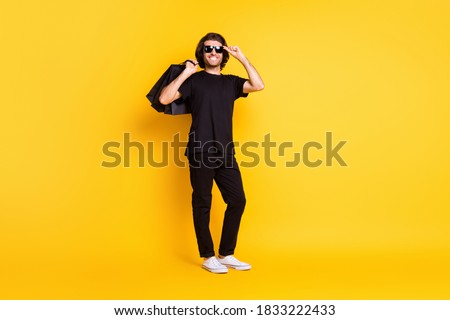 Full length photo of young man hold shopping packages glasses wear black t-shirt pants white sneakers sunglass isolated yellow color background