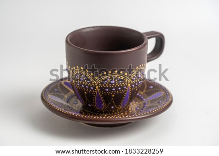Decorative ceramic painted cup and saucer on white background, close up. Decorative porcelain cup and saucer painted with acrylic paints, handwork, dot painting