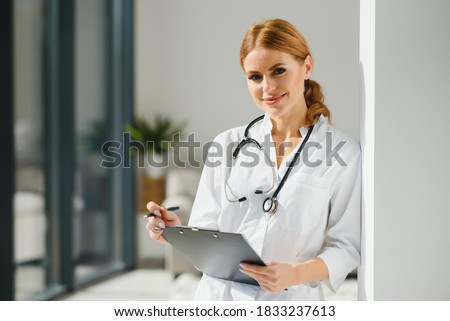 Portrait of smiling young Caucasian woman nurse sit at desk in hospital or private clinic, profile picture of happy positive female doctor GP in white medical uniform at workplace, healthcare concept