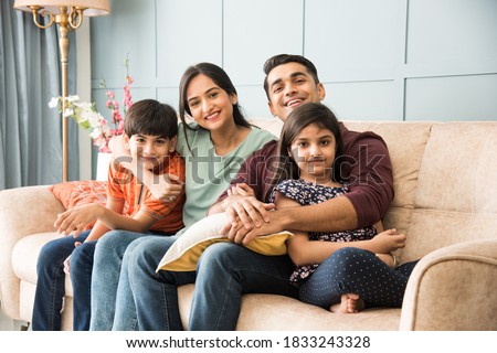 Portrait of happy Indian Asian young family while sitting on sofa, lying on floor or sitting against wall Royalty-Free Stock Photo #1833243328