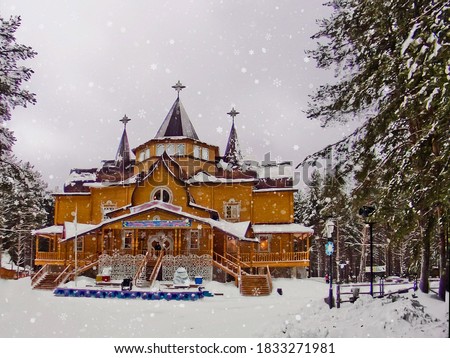 Frontal view Patrimony of Russian Father Frost among fir trees and white snowy field in Veliky Ustyug. Winter fairy-tale wooden palace in the forest among and snowflakes on daylight, cloudy sky.  Royalty-Free Stock Photo #1833271981