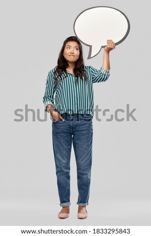 people and communication concept - confused asian young woman holding big blank speech bubble over grey background