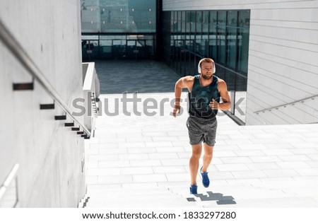 fitness, sport, training and lifestyle concept - young man in headphones running upstairs outdoors