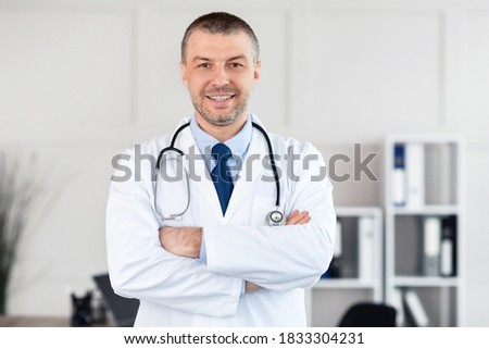 Professional Help. Portrait of smiling confident mature general practitioner standing with folded arms at his office in clinic and posing, looking at camera. Doctor wearing stethoscope and white coat Royalty-Free Stock Photo #1833304231