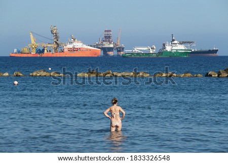 Limassol/Cyprus - 09/20/2020: People in swimwear at the beach with offshore oil and gas exploration and ships and drilling rigs in the background