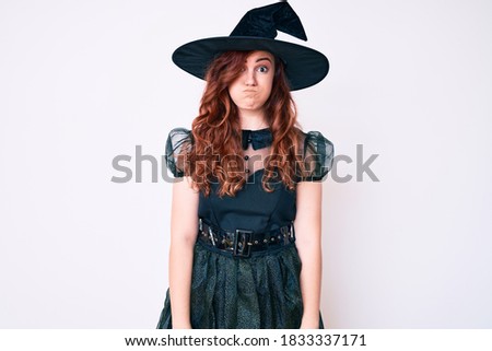 Young beautiful woman wearing witch halloween costume puffing cheeks with funny face. mouth inflated with air, crazy expression. 