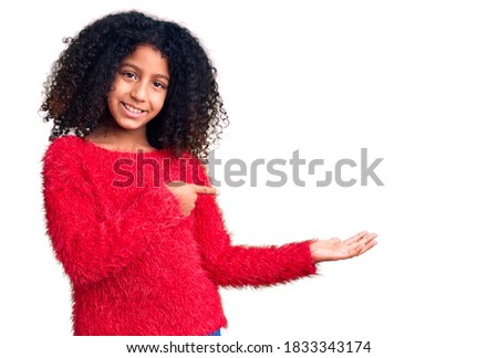 African american child with curly hair wearing casual winter sweater amazed and smiling to the camera while presenting with hand and pointing with finger. 