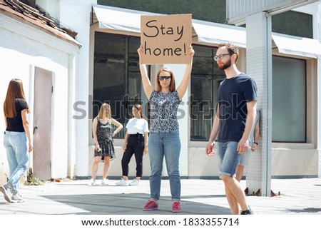 Stay home. Dude with sign - woman stands protesting things that annoy her. Solo demonstration right to talk free on the street with sign. Opinion heard by public. Social life, COVID, healthcare.