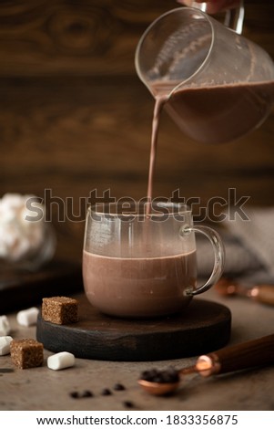 hot sweet chocolate cocoa is poured into a glass cup on a wooden table