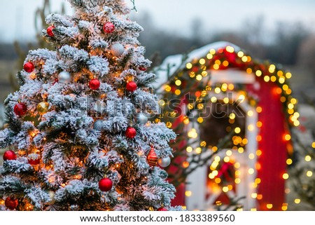 Fir tree decorated with snow and toy red glass balls and light bulbs for Christmas and New Year celebration
