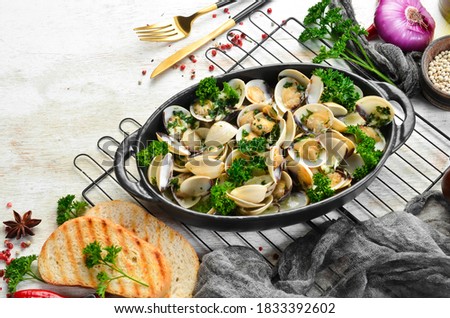 Boiled shellfish in shells with garlic and parsley in a black plate. Seafood. Top view. Free space for text.
