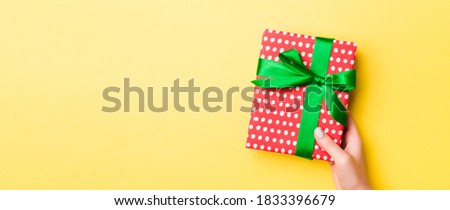 Woman arms holding gift box with colored ribbon on yellow table background, top view and copy space for you design.