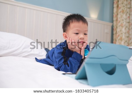 Cute Asian toddler boy child lying on his stomach while playing game, watching cartoon, using tablet pc computer, Gadget addicted children, Learning Tablet for Kids - Selective focus