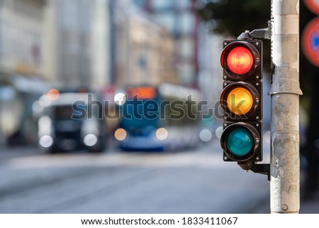 blurred view of city traffic with traffic lights, in the foreground a semaphore with a red and yellow light