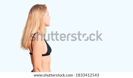 Young beautiful blonde woman wearing bikini looking to side, relax profile pose with natural face and confident smile. 