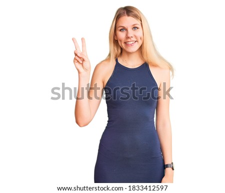 Young beautiful blonde woman wearing casual dress showing and pointing up with fingers number two while smiling confident and happy. 