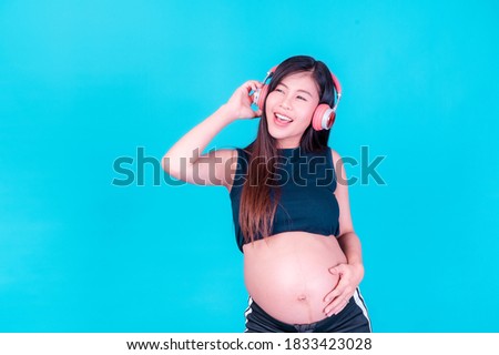 Asian beautiful pregnant woman stands relaxed and enjoys listening to music on headphones connected to the internet