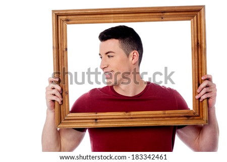 Smiling guy holding wooden picture frame and looking away