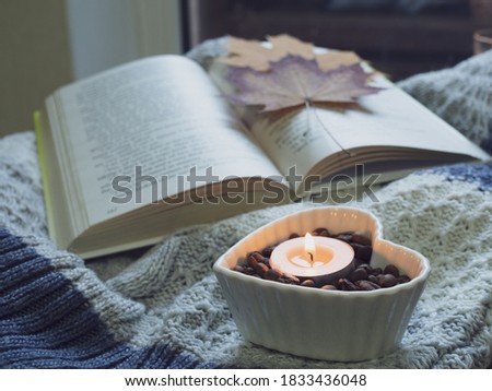 A book with orange maple leaves, a grey sweater, candle with coffee beans in a bowl. Focus on a candle. Brown wooden table. Autumn mood.  Royalty-Free Stock Photo #1833436048