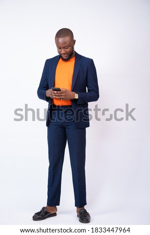 young african man wearing a suit using his phone, texting and chatting concept, standing against a white background Royalty-Free Stock Photo #1833447964