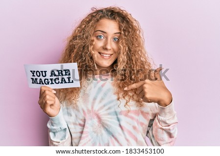 Beautiful caucasian teenager girl holding you are magical banner pointing finger to one self smiling happy and proud 