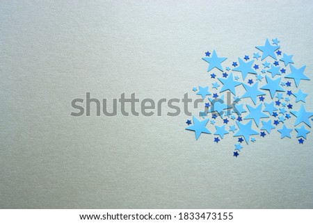 A lot of blue smooth plastic confetti stars. Different sizes. Silver shimmer background. Celebration. Christmas. Festive.