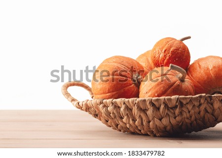 Orange round pumpkins in wicker basket on light wooden table. Copy space. Happy Halloween.