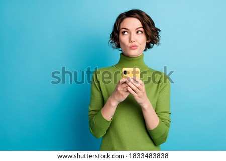 Photo of minded unsure girl use smartphone want type text dont know what about wear green style stylish trendy pullover isolated blue color background