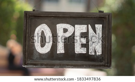 Open sign inscribed in chalk on board in outside setting.
