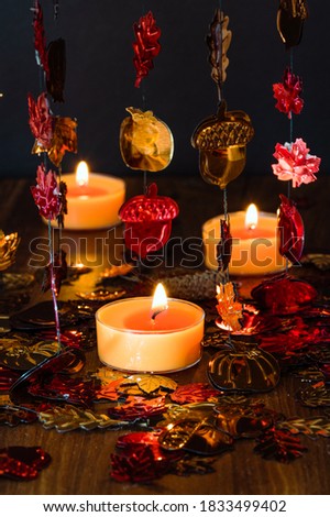 Vertical photo of an artificial autumnal leaves and burning orange candles over the dark background