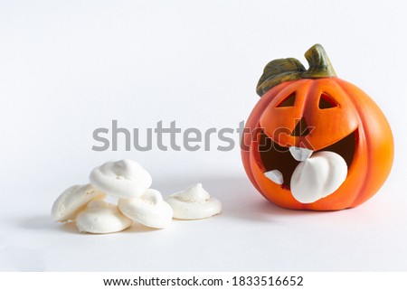 An orange cheerful pumpkin eats a meringue ghost, next to a handful of meringue on a white background. Halloween, All Saints Day, traditional autumn holiday. Trick or treat. Postcard. Copy space.