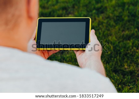 male hands holding an electronic tablet mock-up for your text message or information content, against the background of green nature