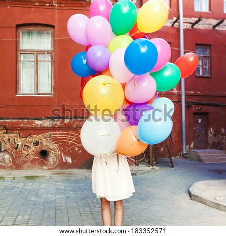 girl in white summer dress hides herself behind a bunch of balloons