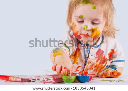The little boy dips his finger in the paint. The body and clothes are smeared with paints
