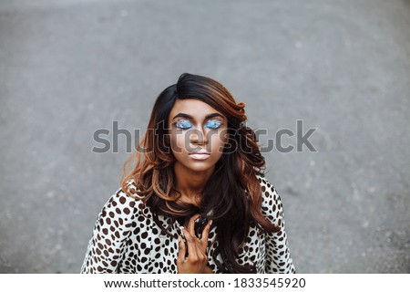 Cropped outroor shot of a black african girl with fantasy pop art make-up wearing polka dot fashionable jacket, with curly long hairstyle. Minimalistic grey background with copy space for your text