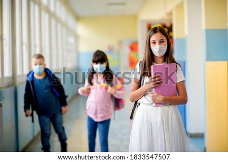 Elementary school students walking down the hallway in between classes. They wearing protective face masks during the corona virus outbreak to protect themselves